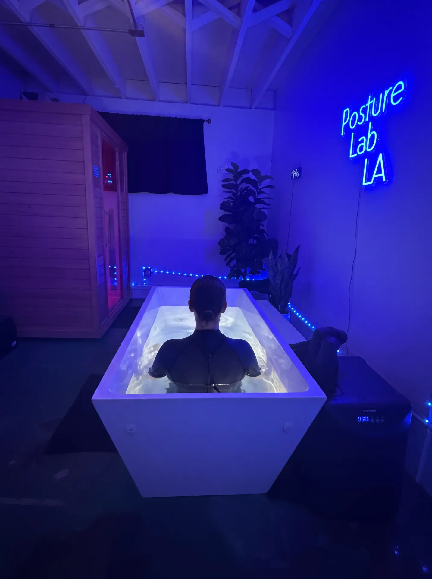 Woman in the cold plunge beside the infrared sauna under the Posture Lab LA neon sign in Santa Monica